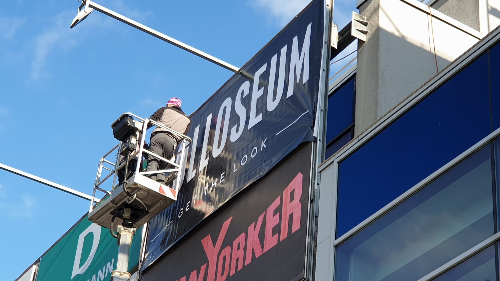 Werbeplane drucken lassen Österreich – Montage eines großformatigen Werbebanner an Einkaufszentrum-Fassade